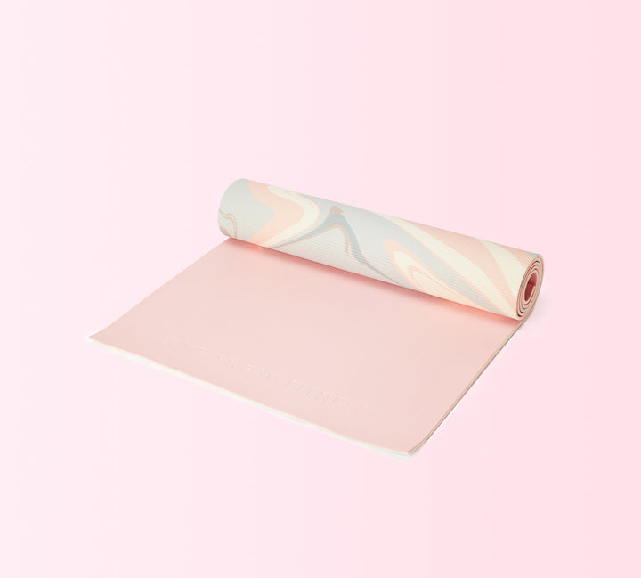 A rolled out pink yoga mat with a textured surface, partially unrolled to reveal a shiny, reflective end.