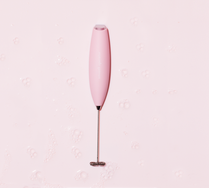 A pink electric whisk with a metal stand on a light background. Smooth Operator